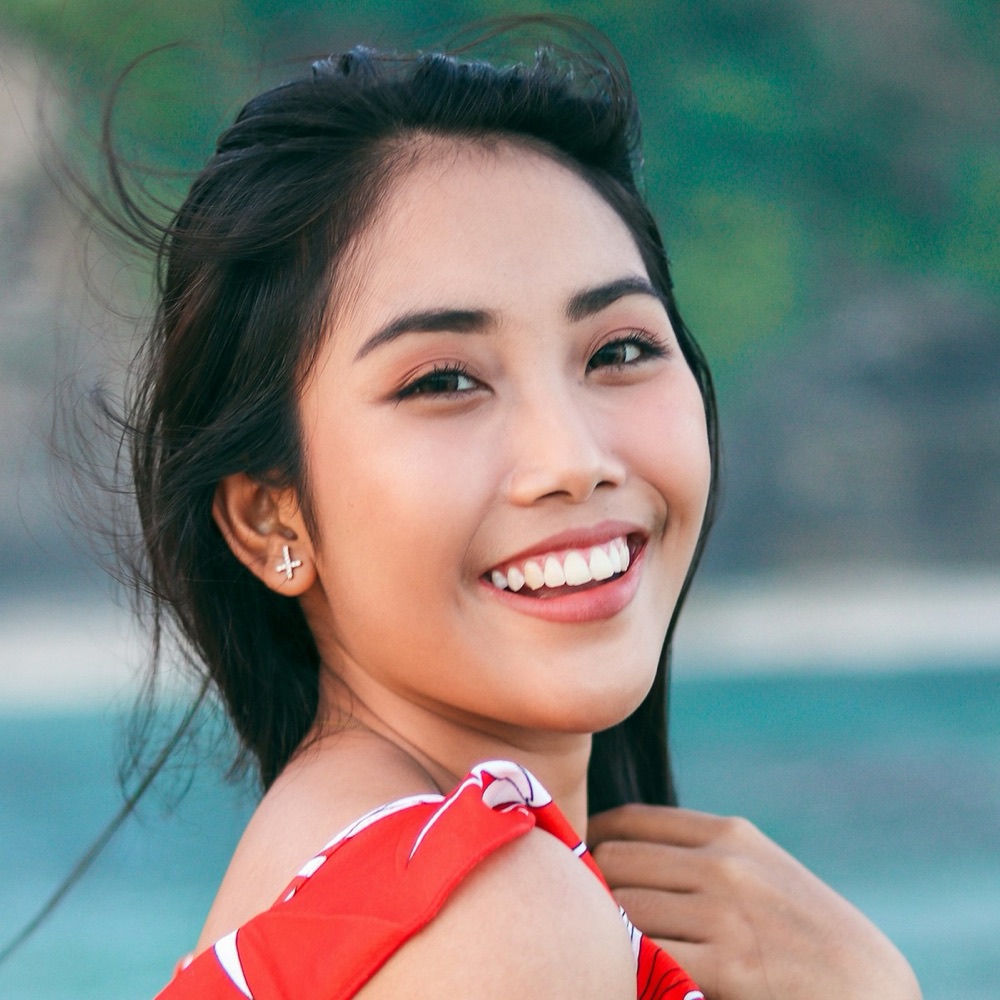 Maya, smiling in a red top by the sea