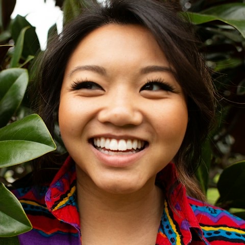 Nadia, laughing among green leaves in a bright patterned shirt